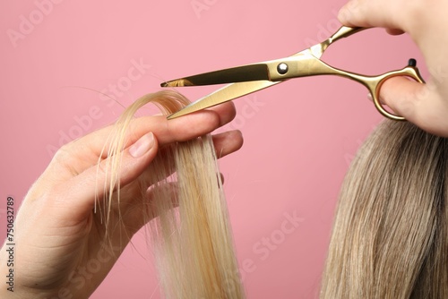 Hairdresser cutting client's hair with scissors on pink background, closeup