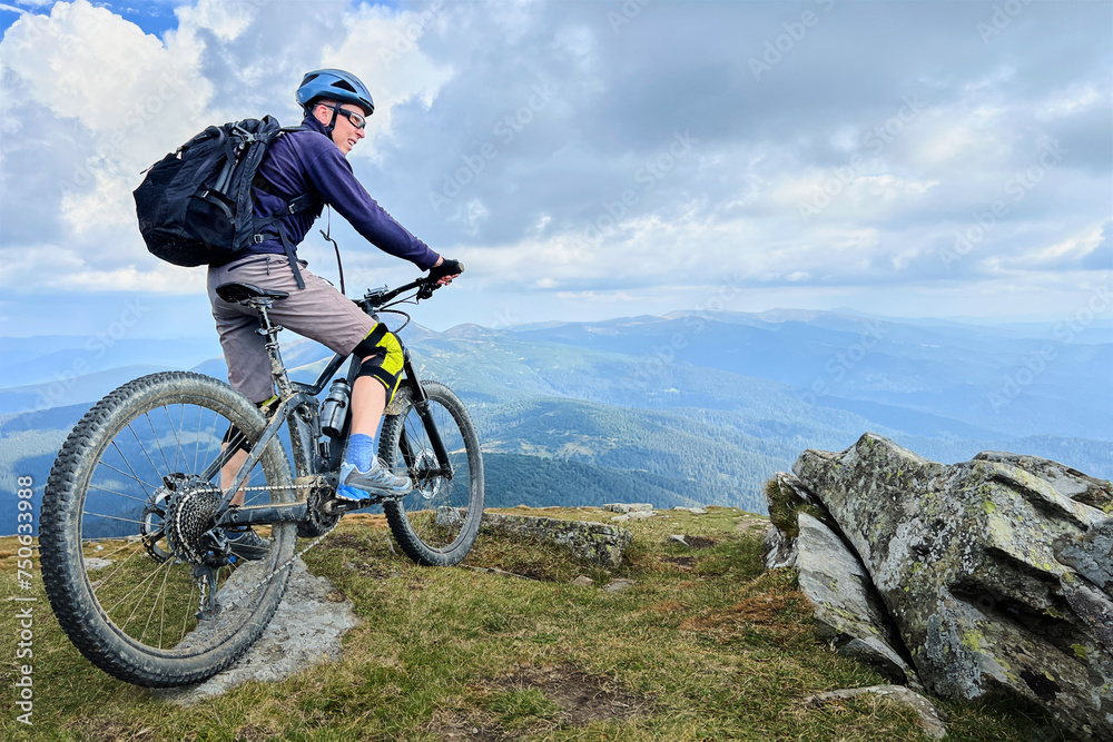 Cyclist man riding electric bike outdoors. Male tourist resting on the top of hill, enjoying beautiful mountain landscape, wearing helmet and backpack. Concept of active leisure. Cyclist man riding electric bike outdoors. Male tourist resting on the top of hill, enjoying beautiful mountain landscape, wearing helmet and backpack. Concept of active leisure.