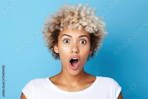 A beautiful African American woman with a short haircut is surprised on a blue background. 