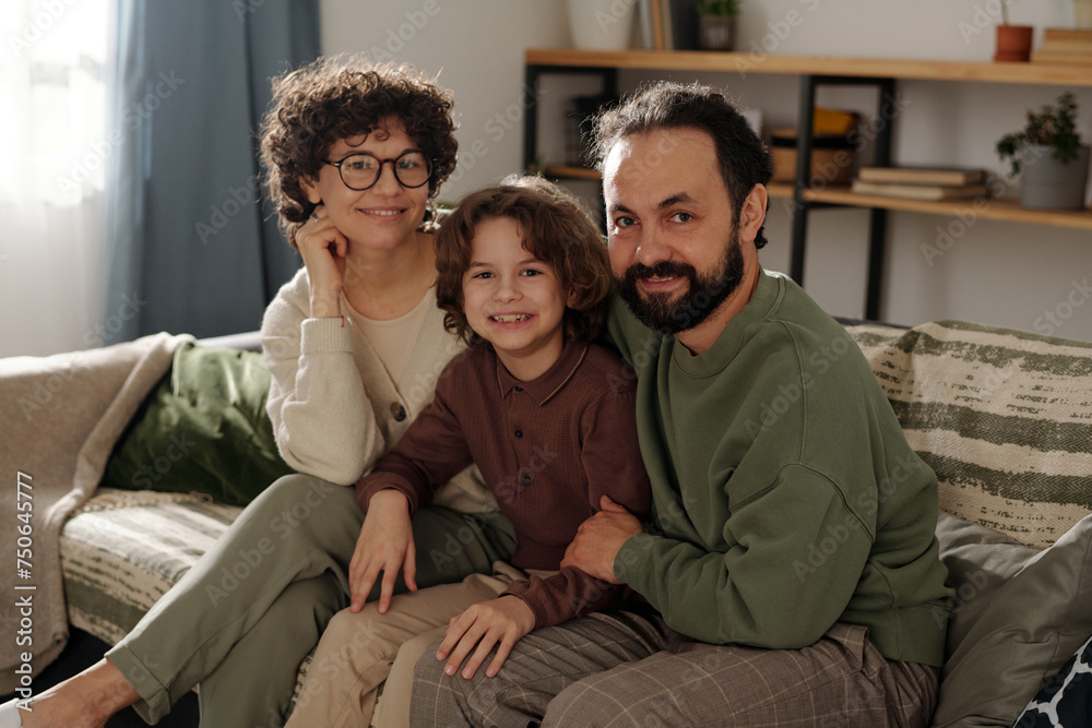 Happy and affectionate family members looking at camera with smiles while sitting on couch in living room of new apartment