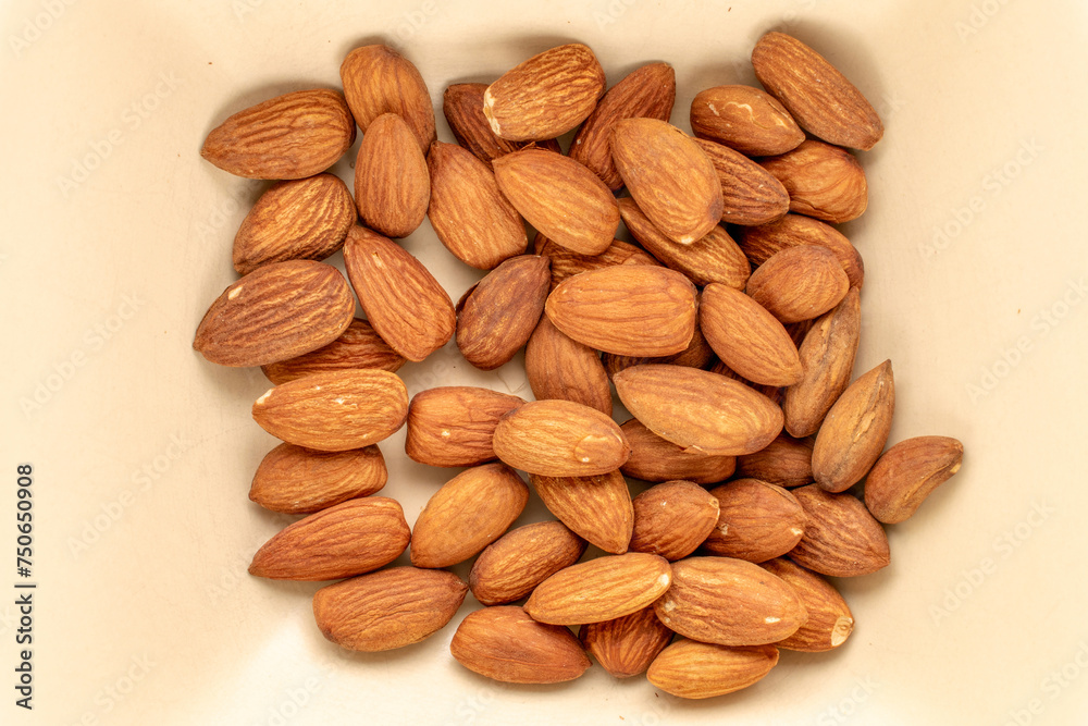 A small amount of roasted almonds in a ceramic dish, macro, top view. A small amount of roasted almonds in a ceramic dish, macro, top view.
