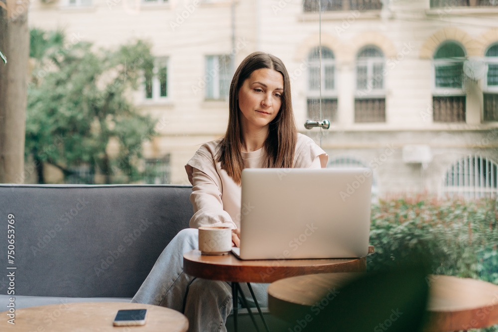 Brunette business woman working remotely using laptop while sitting in a cozy cafe. Brunette business woman working remotely using laptop while sitting in a cozy cafe.