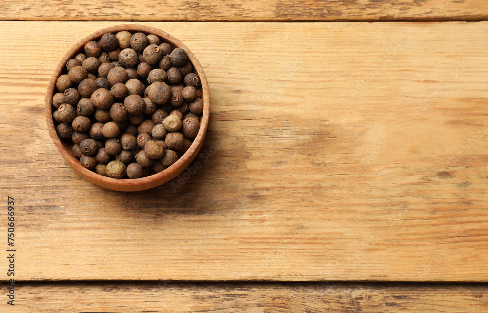 Dry allspice berries (Jamaica pepper) in bowl on wooden table, top view. Space for text Dry allspice berries (Jamaica pepper) in bowl on wooden table, top view. Space for text