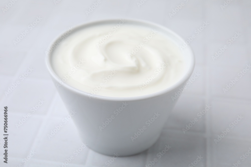 Delicious natural yogurt in bowl on white tiled table, closeup Delicious natural yogurt in bowl on white tiled table, closeup