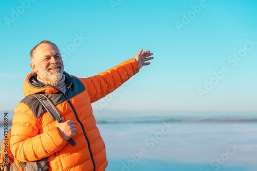 elderly  mature man enjoying life at full by travelling around world sitting on the top of mountains against sky and clouds on cold sunny winter soring day. Travel Lifestyle concept photo