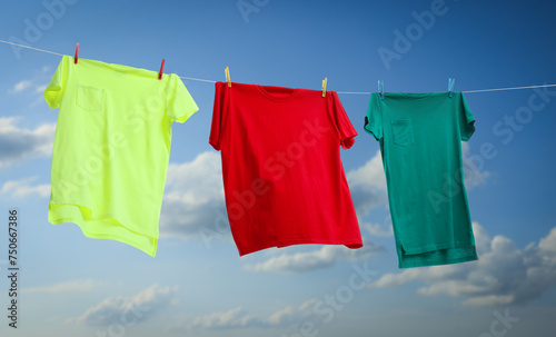Colorful t-shirts drying on washing line against blue sky, banner design