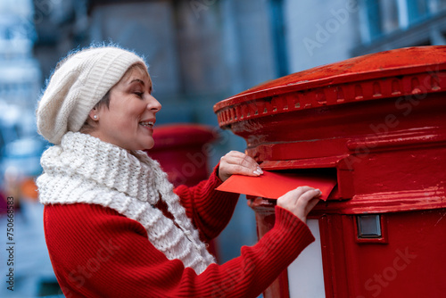 Canvas Print woman in a red coat and white hat  putting a card in the red postbox and walking