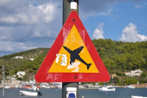 Bright warning sign next to Skiathos airport runway, Greece, informing pedestrians of low flying overhead airplanes. 