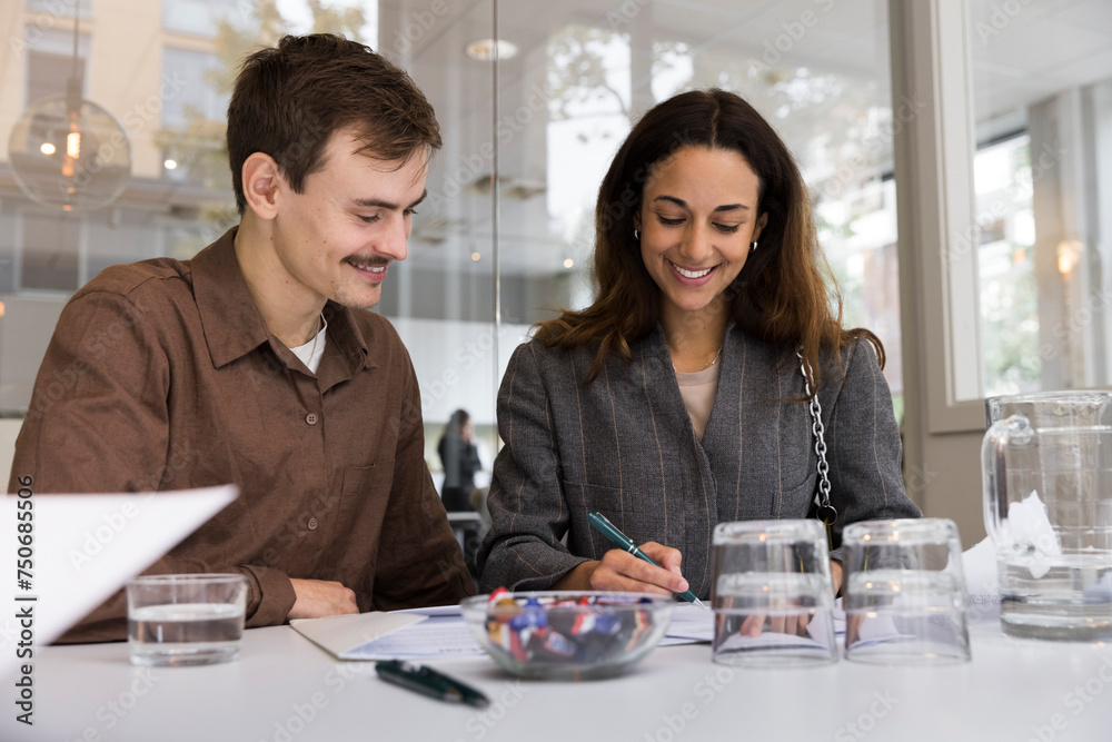 Man looking at smiling woman signing agreement at desk in real estate office Man looking at smiling woman signing agreement at desk in real estate office