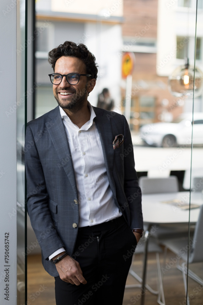 Smiling male real estate agent leaning on glass door in office Smiling male real estate agent leaning on glass door in office
