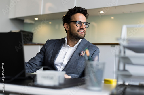 Thoughtful male real estate agent sitting at desk in office photo
