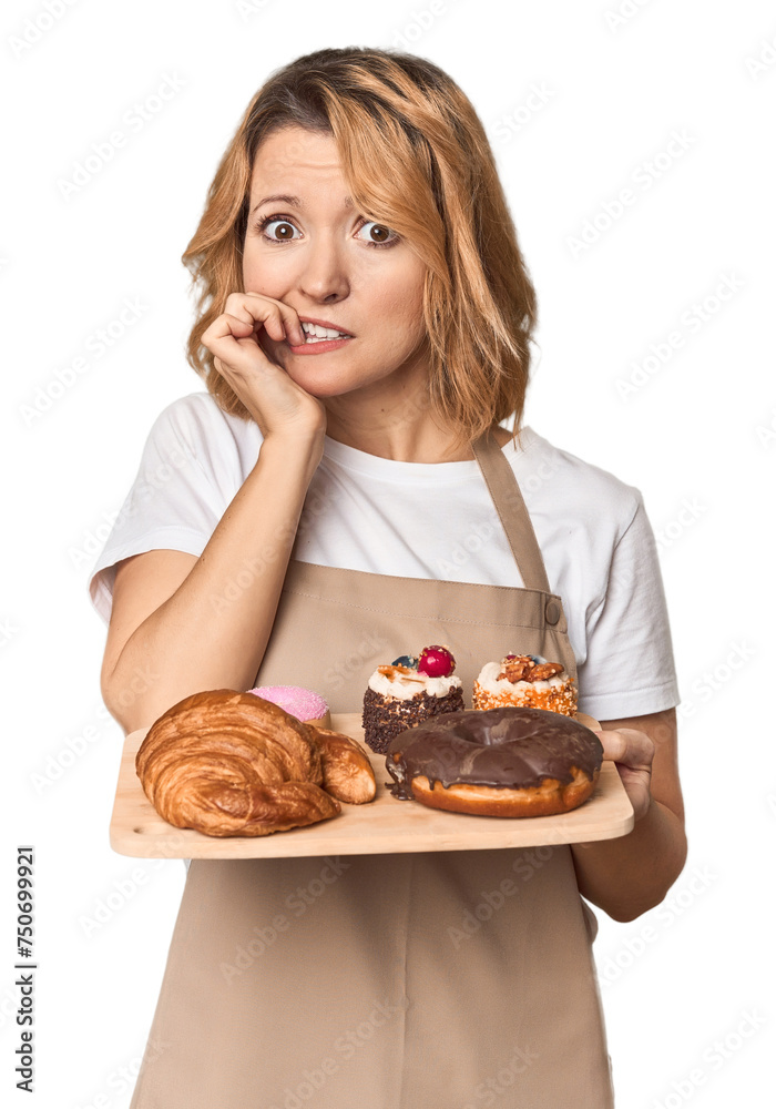 Middle-aged Caucasian woman baker with pastries biting fingernails, nervous and very anxious. Middle-aged Caucasian woman baker with pastries biting fingernails, nervous and very anxious.
