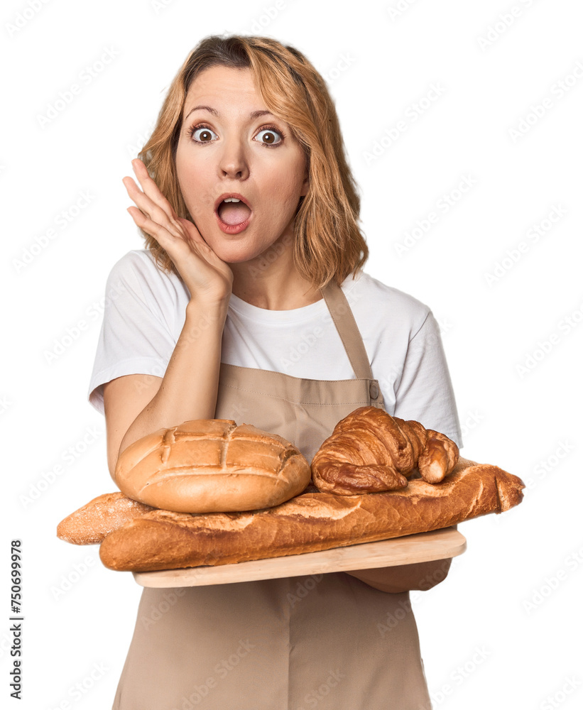 Middle-aged Caucasian woman baker with bread tray surprised and shocked. Middle-aged Caucasian woman baker with bread tray surprised and shocked.