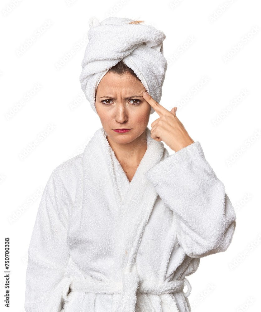 Caucasian woman in bathrobe and towel pointing temple with finger, thinking, focused on a task. Caucasian woman in bathrobe and towel pointing temple with finger, thinking, focused on a task.