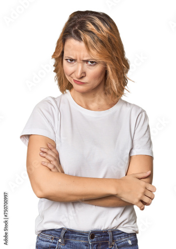 Blonde middle-aged Caucasian woman in studio frowning face in displeasure, keeps arms folded. © Asier