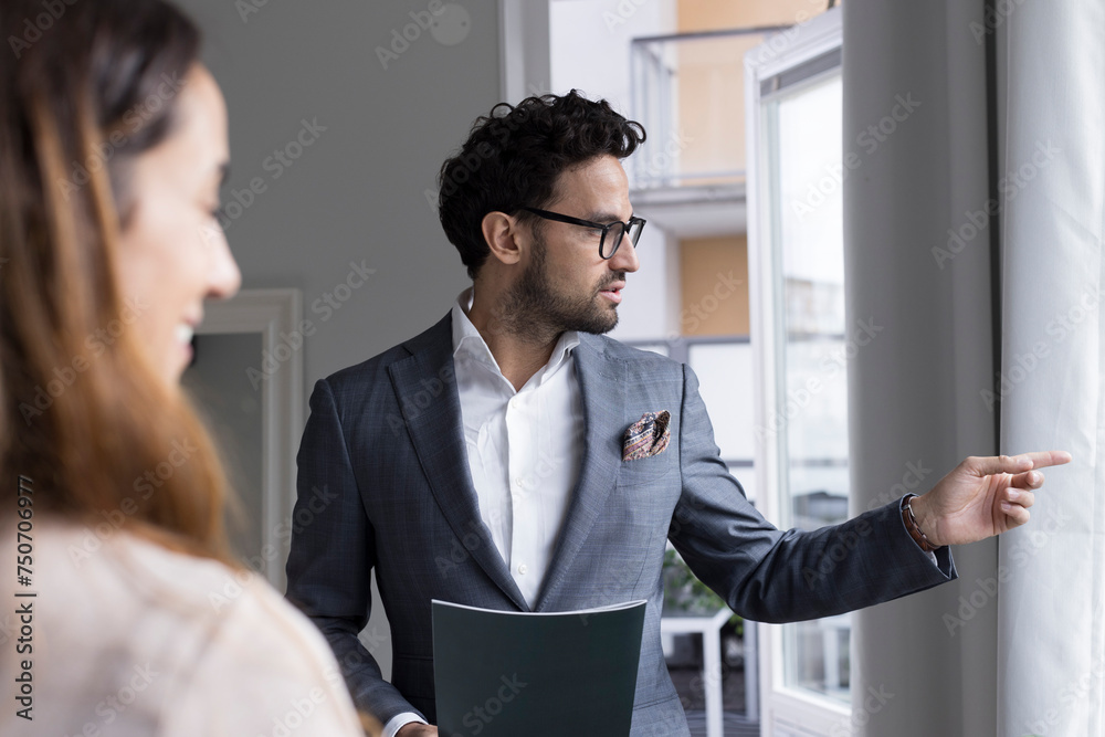 Male real estate agent pointing while talking with female client at home Male real estate agent pointing while talking with female client at home