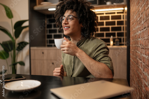 Curly-haired young man sitting at the table and having coffee