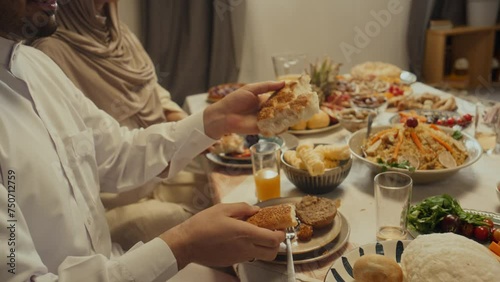 Side tilt footage of smiling bearded muslim man sharing flatbread or pita with family members during festive dinner celebrating Eid al-Fitr at home photo