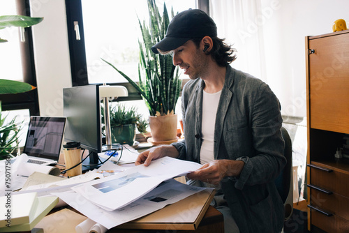 Male architect analyzing blueprint while sitting at desk in home office photo