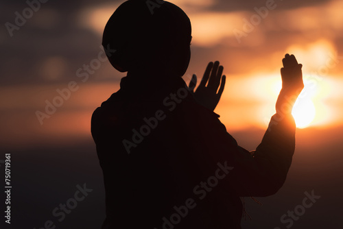Muslim woman prayer praying with hands up open doing dua at sunset worship Allah.
