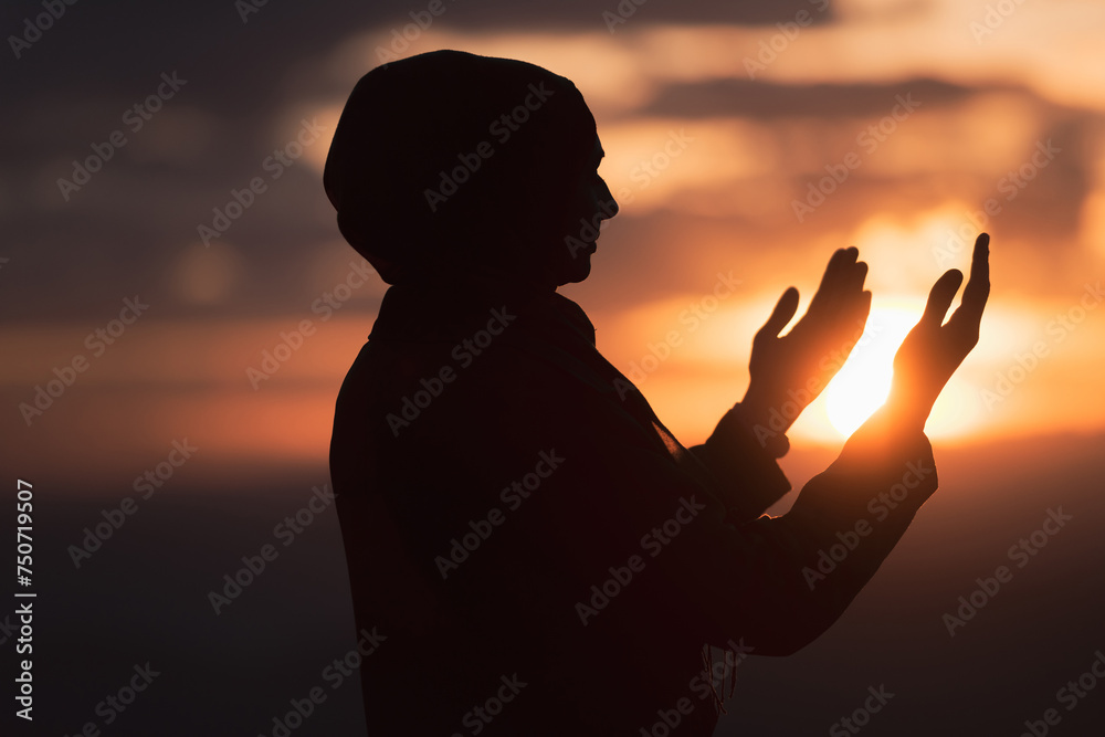 Muslim woman prayer praying with hands up open doing dua at sunset worship Allah.
