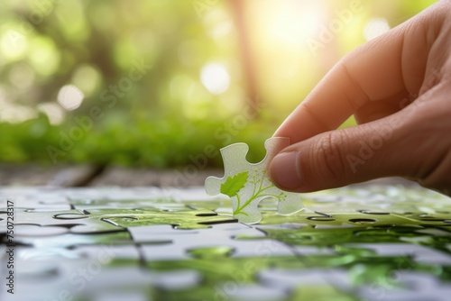 Hand placing a transparent puzzle piece into a larger puzzle depicting a green environment, with a blurred natural landscape, the idea of sustainable business practices photo
