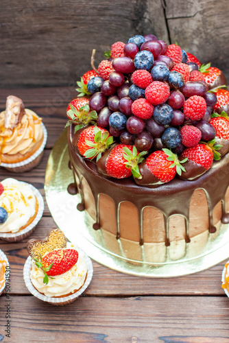 Chocolate cake with berries dipped into melted chocolate surrounded by vanilla cupcakes with cream cheese frosting