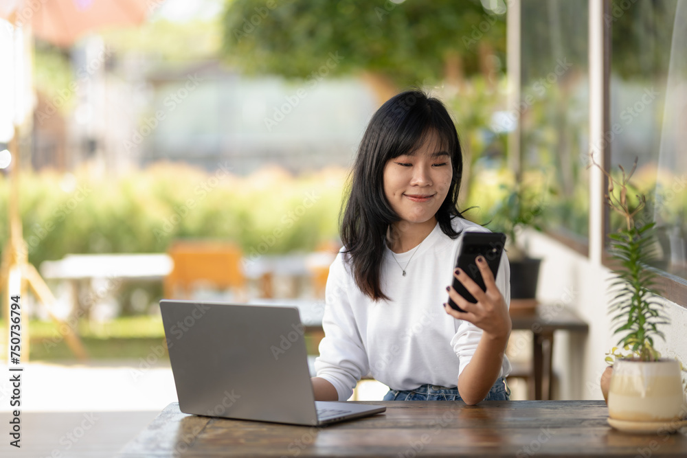 Obraz premium Young Asian woman using smartphone and laptop in outdoor cafe, self-employed