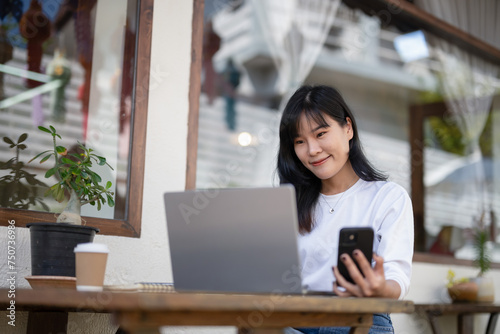 Young Asian woman using smartphone and laptop in outdoor cafe, self-employed
