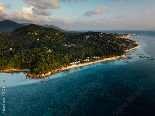 This bird's-eye view reveals a beautiful tropical island. Surrounded by clear turquoise water like glass. The pristine white beaches contrast with the lush greenery of the island's greenery. In the ce
