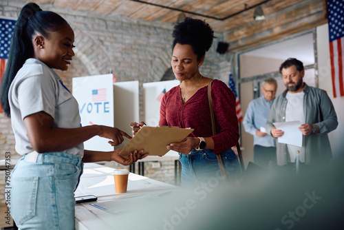 Polling place volunteer assisting black woman to sign up for voting during USA elections.