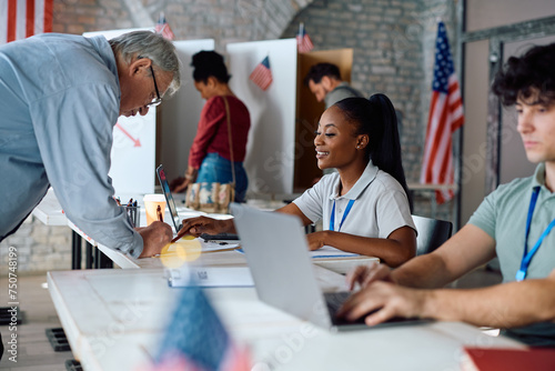 Εκτύπωση καμβά Senior US citizen signing up for voting with help of black female volunteer at polling place