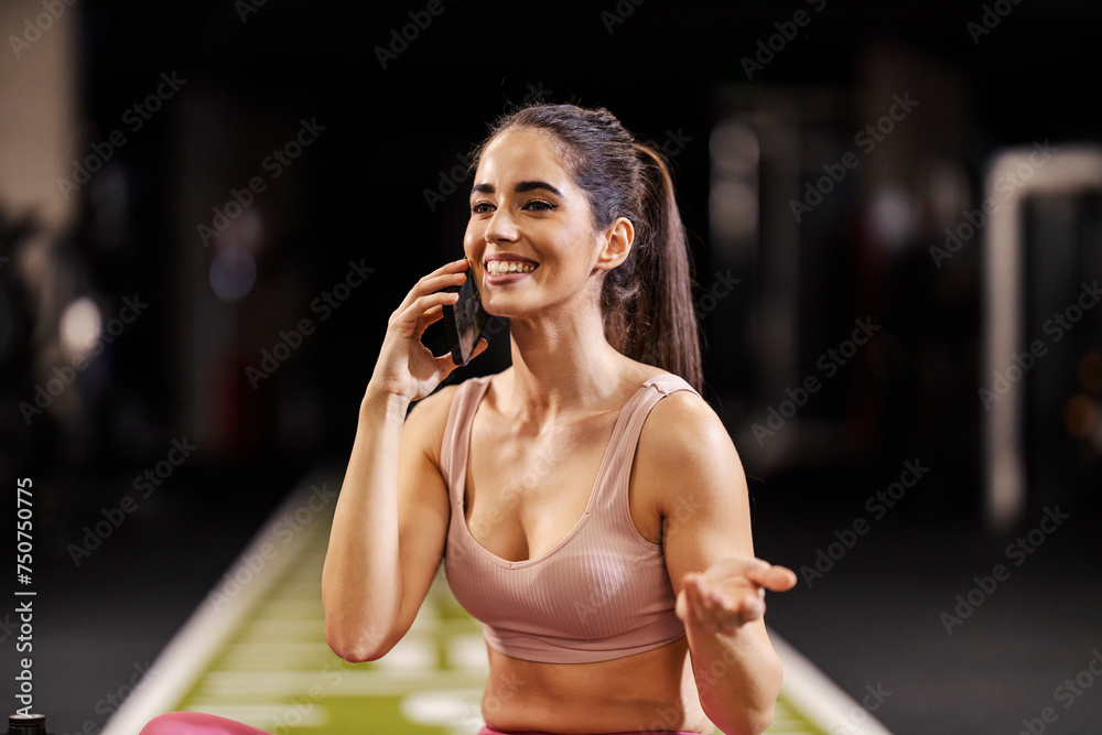 Portrait of a sportswoman talking on a cellphone in a gym. - obrazy, fototapety, plakaty 