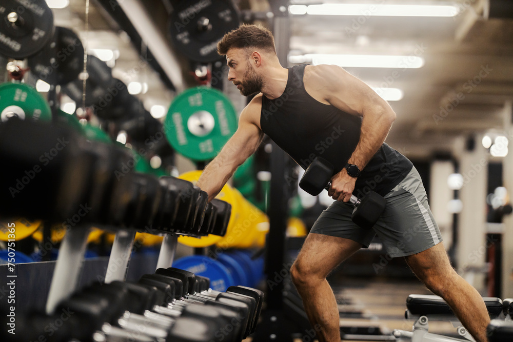 Fit strong man is practicing with dumbbell in a gym. Fit strong man is practicing with dumbbell in a gym.