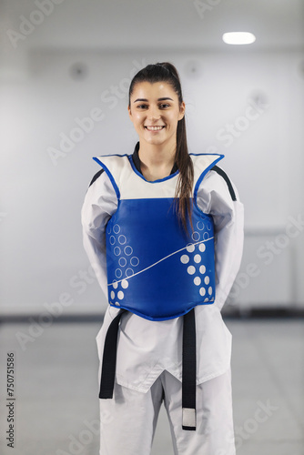 Portrait of taekwondo girl in dobok with black belt standing at martial art school and smiling at the camera.
