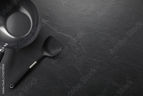 Black metal wok and spatula on dark textured table, top view. Space for text