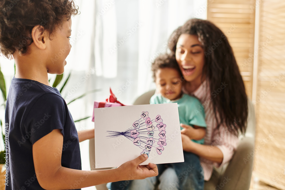 focus on little african american boy giving gift and postcard to his mother that holding his brother focus on little african american boy giving gift and postcard to his mother that holding his brother