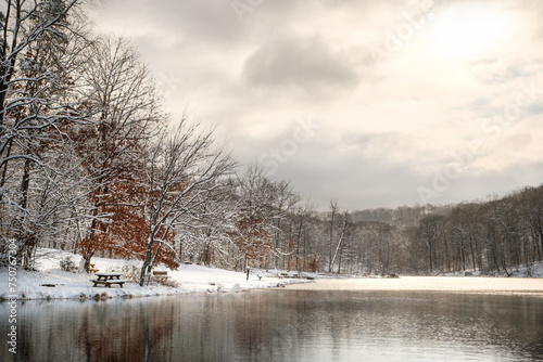A wide angle view of a small lake in Indiana in the middle of winter on a snowy day with a mostly cloudy sky. The sun is bursting through the clouds and there are nice reflections on the water.  © Douglas