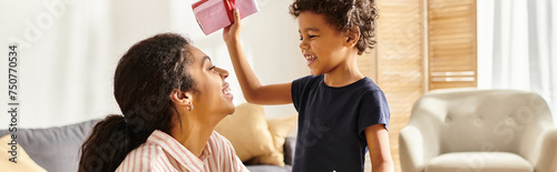 cute african american boy giving present and postcard to his jolly mother, modern parenting, banner