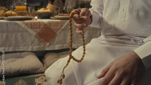 Side tilt footage of young Arab muslim man in traditional apparel using tasbih while performing namaz at home on Eid al-Fitr day photo