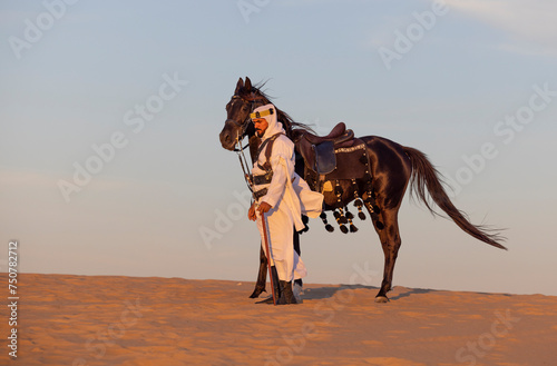 Man in traditional Saudi clothing in a desert with his black stallion