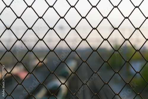 Cells of a wire fence in the evening against the background of a railway in a blur