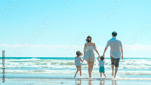 Rear view of a happy family walking on the beach in the summer with a clear sky.