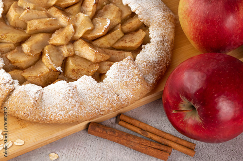 On a gray table on a wooden board there is a galette with apples and cinnamon.