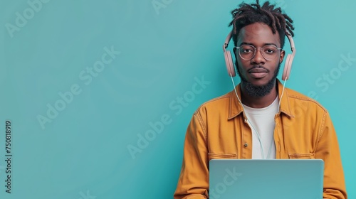 Focused man in a yellow jacket working on a laptop with headphones on a blue background. photo