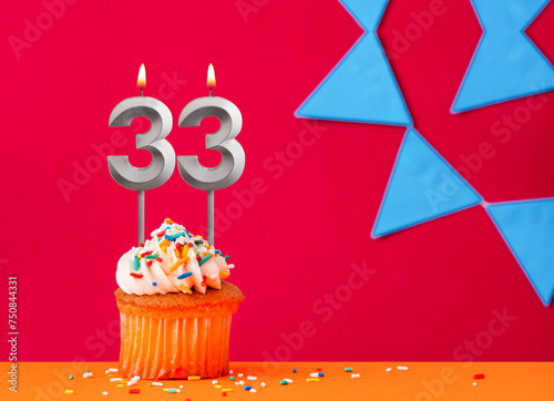 Birthday cupcake with candle number 33 on a red background with blue pennants