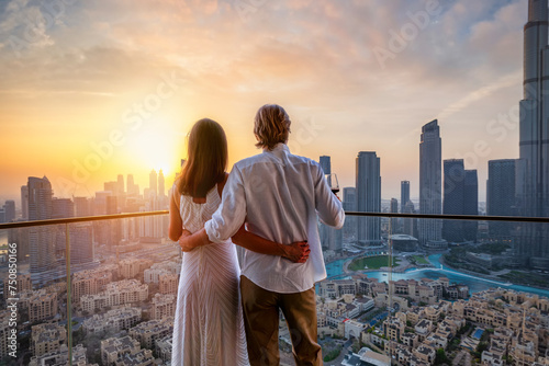 A hugging couple enjoys the beautiful sunset behind the skyline of Downtown Dubai, UAE
