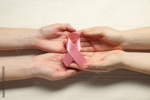 Women holding pink ribbon at white wooden table, top view. Breast cancer awareness