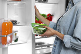 Young woman taking container with vegetables out of refrigerator, closeup