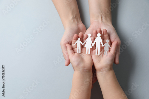 Parents and child holding paper family figures on gray background, top view. Space for text